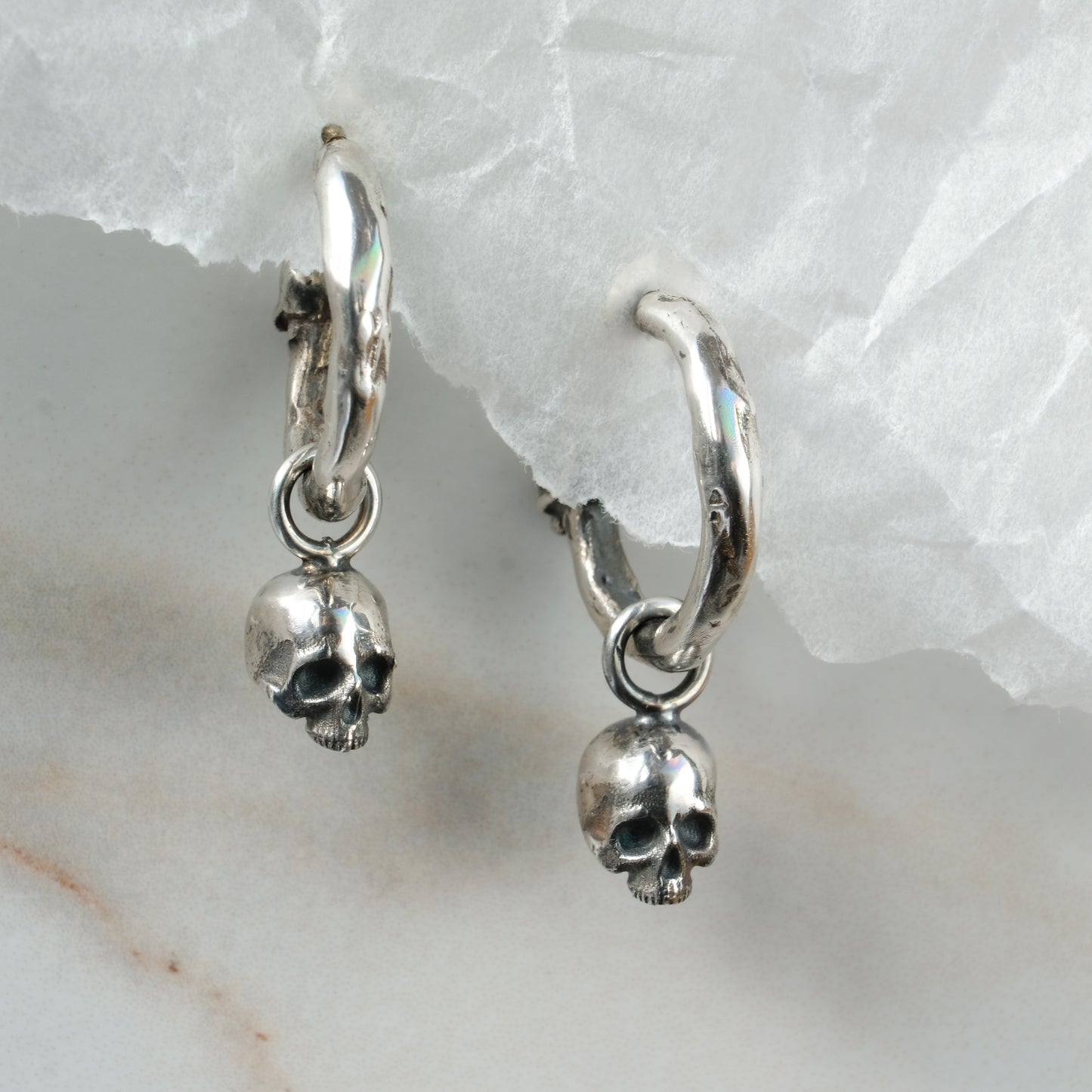 Molten style sterling silver earrings with hidden skull stoppers and skulls hanging. Made in London by Charlie Shires