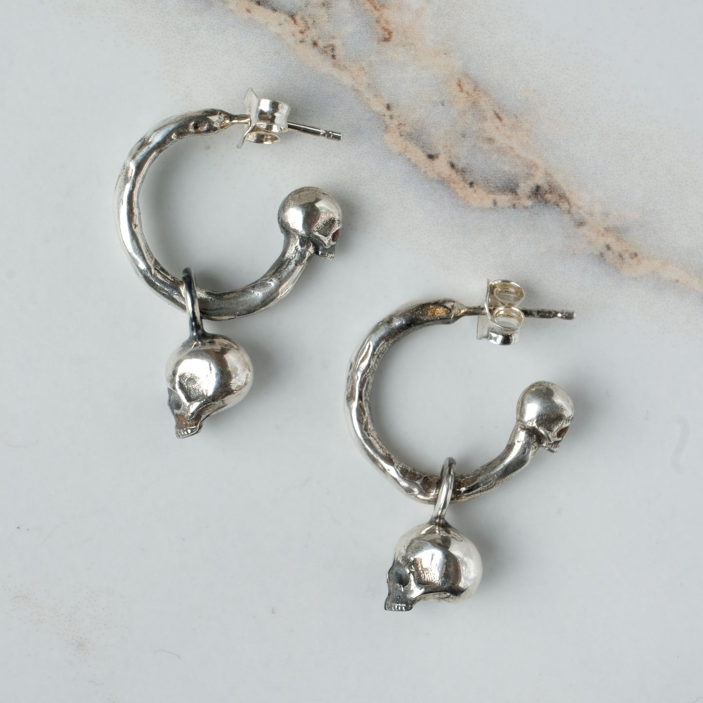 Molten style sterling silver earrings with hidden skull stoppers and skulls hanging. Made in London by Charlie Shires