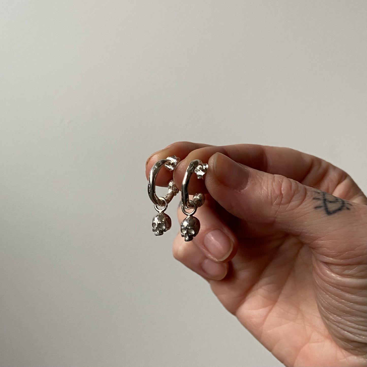 Molten style sterling silver earrings with hidden skull stoppers and skulls hanging. Made in London by Charlie Shires