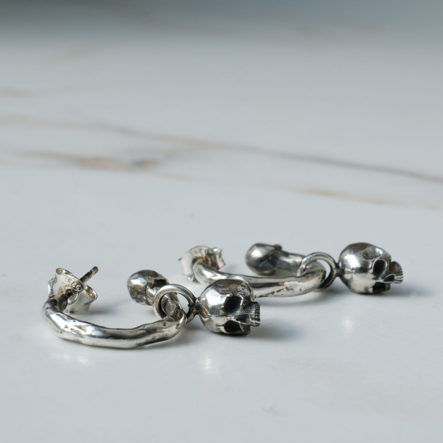 Molten style sterling silver earrings with hidden skull stoppers and skulls hanging. Made in London by Charlie Shires
