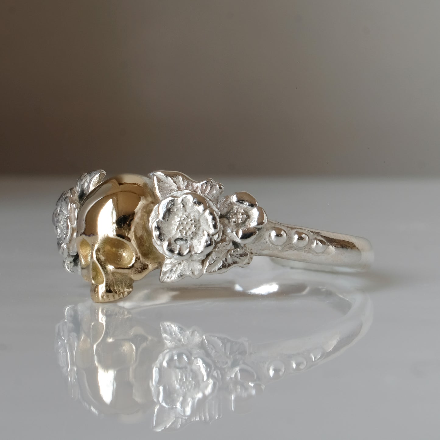 Sterling silver ring with central 9ct yellow gold skull and flower and leaves cascading down band. Handmade in London by Charlie Shires