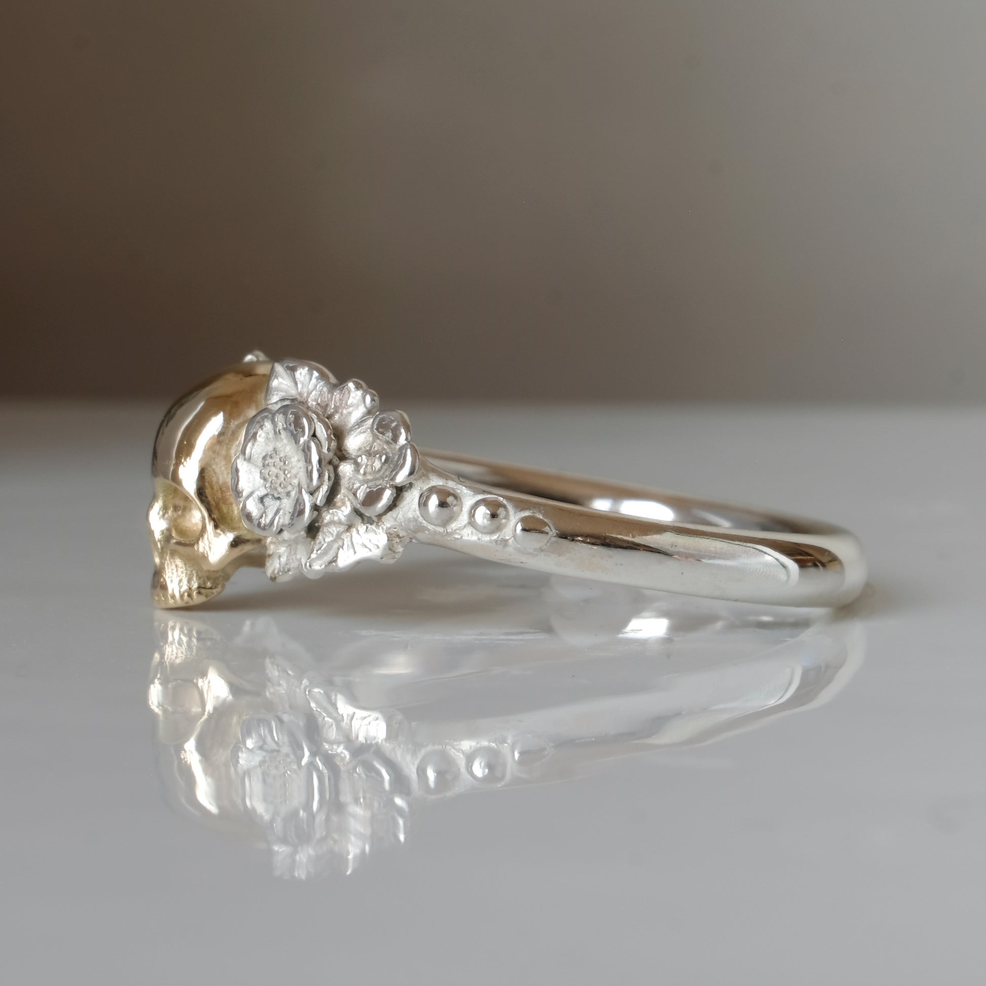 Sterling silver ring with central 9ct yellow gold skull and flower and leaves cascading down band. Handmade in London by Charlie Shires