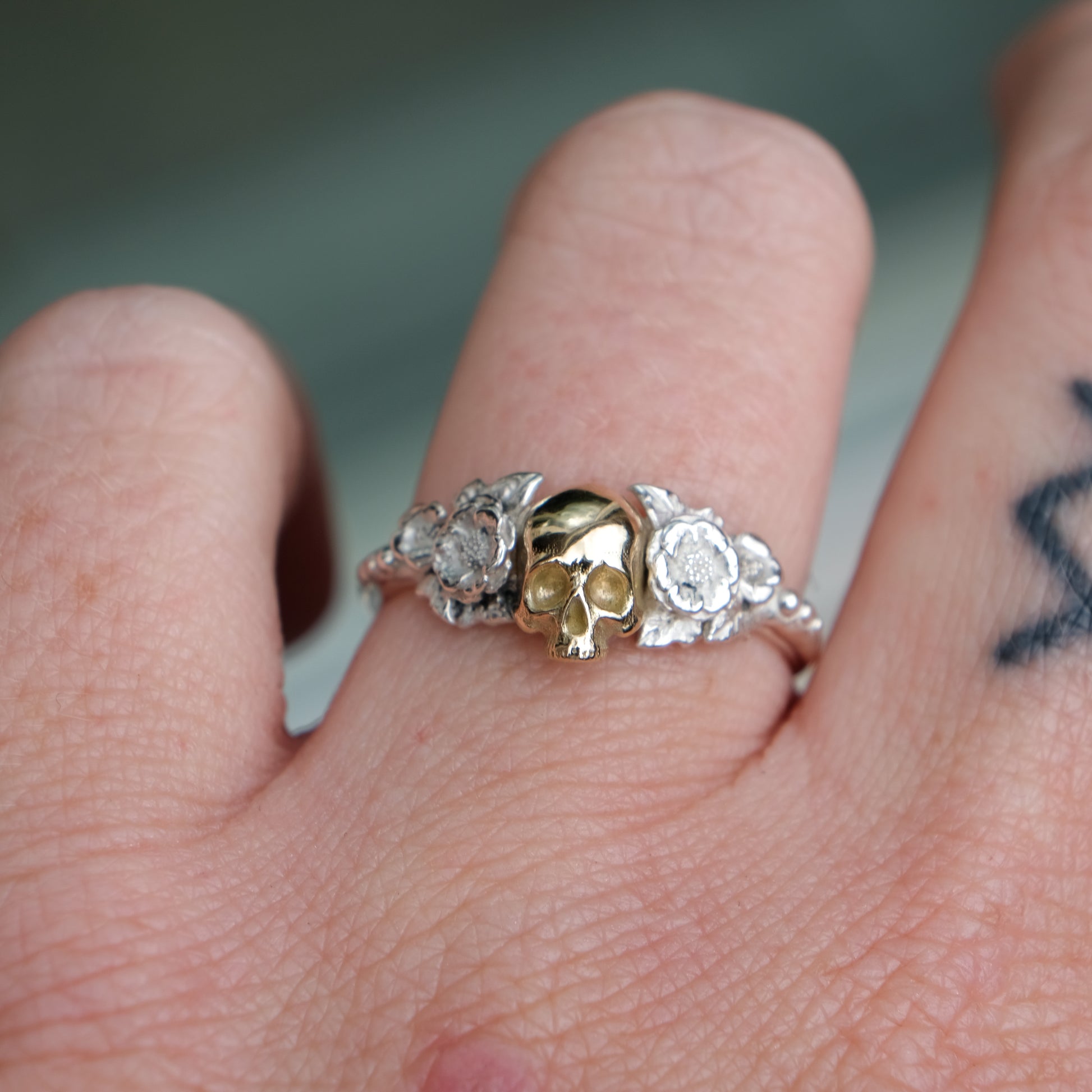 Sterling silver ring with central 9ct yellow gold skull and flower and leaves cascading down band. Handmade in London by Charlie Shires
