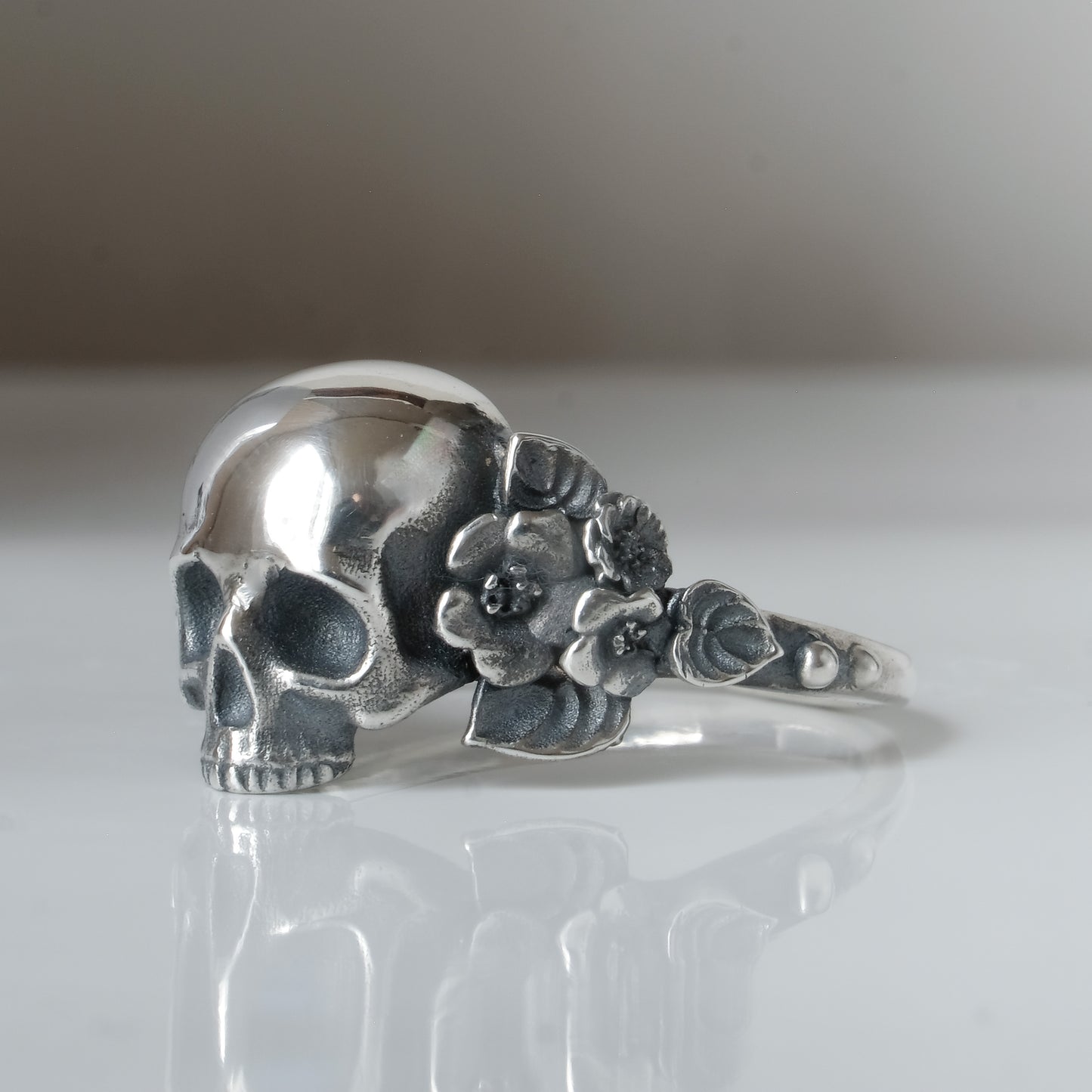 Sterling silver ring with central large skull and flower and leaves cascading down band. Handmade in London by Charlie Shires