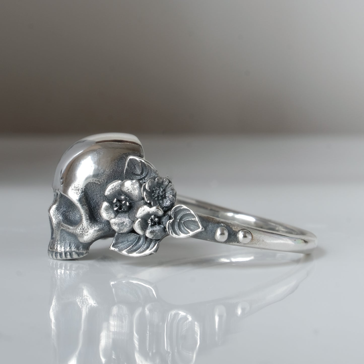 Sterling silver ring with central large skull and flower and leaves cascading down band. Handmade in London by Charlie Shires