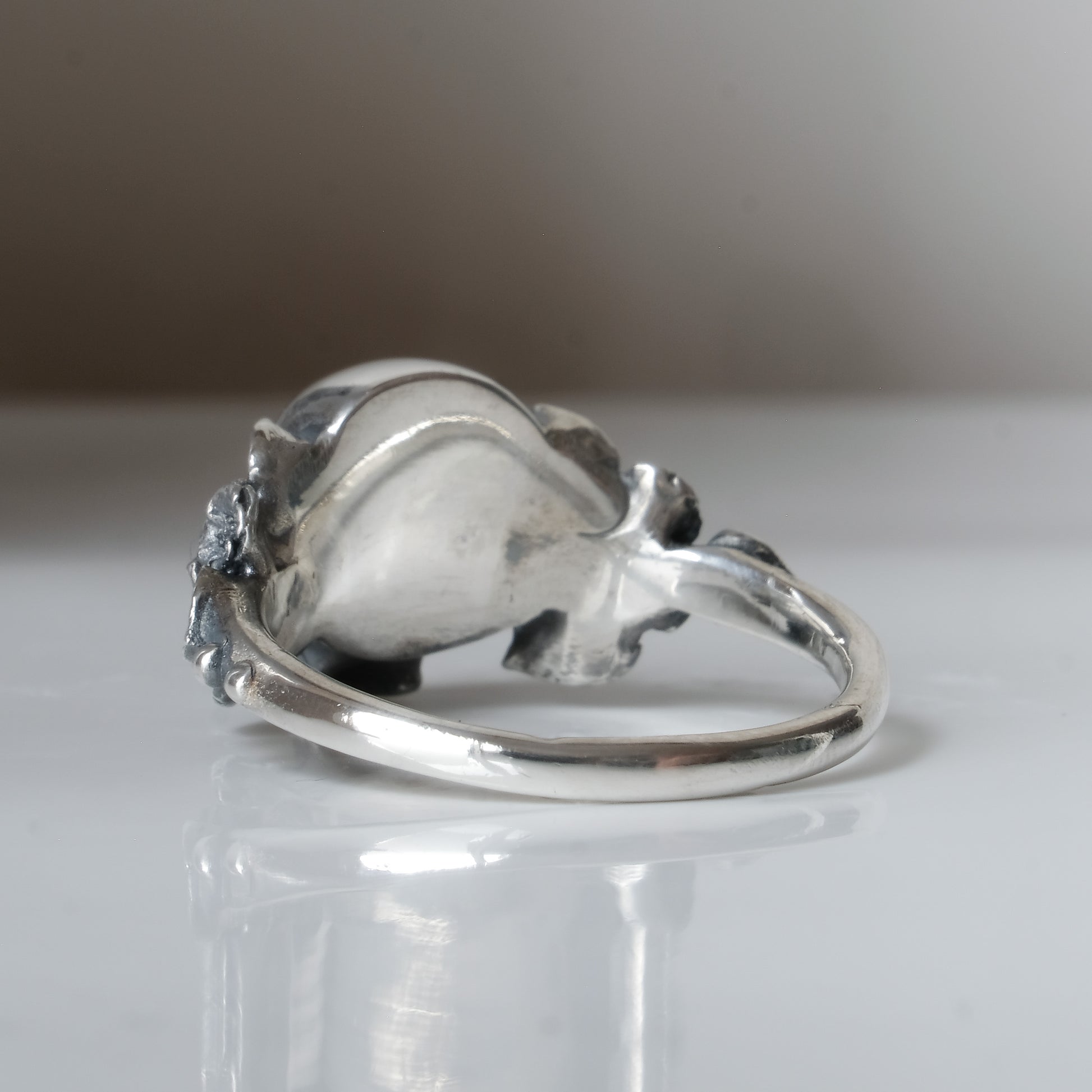 Sterling silver ring with central large skull and flower and leaves cascading down band. Handmade in London by Charlie Shires