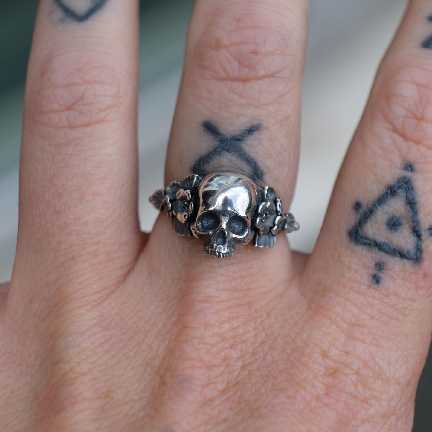 Sterling silver ring with central large skull and flower and leaves cascading down band. Handmade in London by Charlie Shires