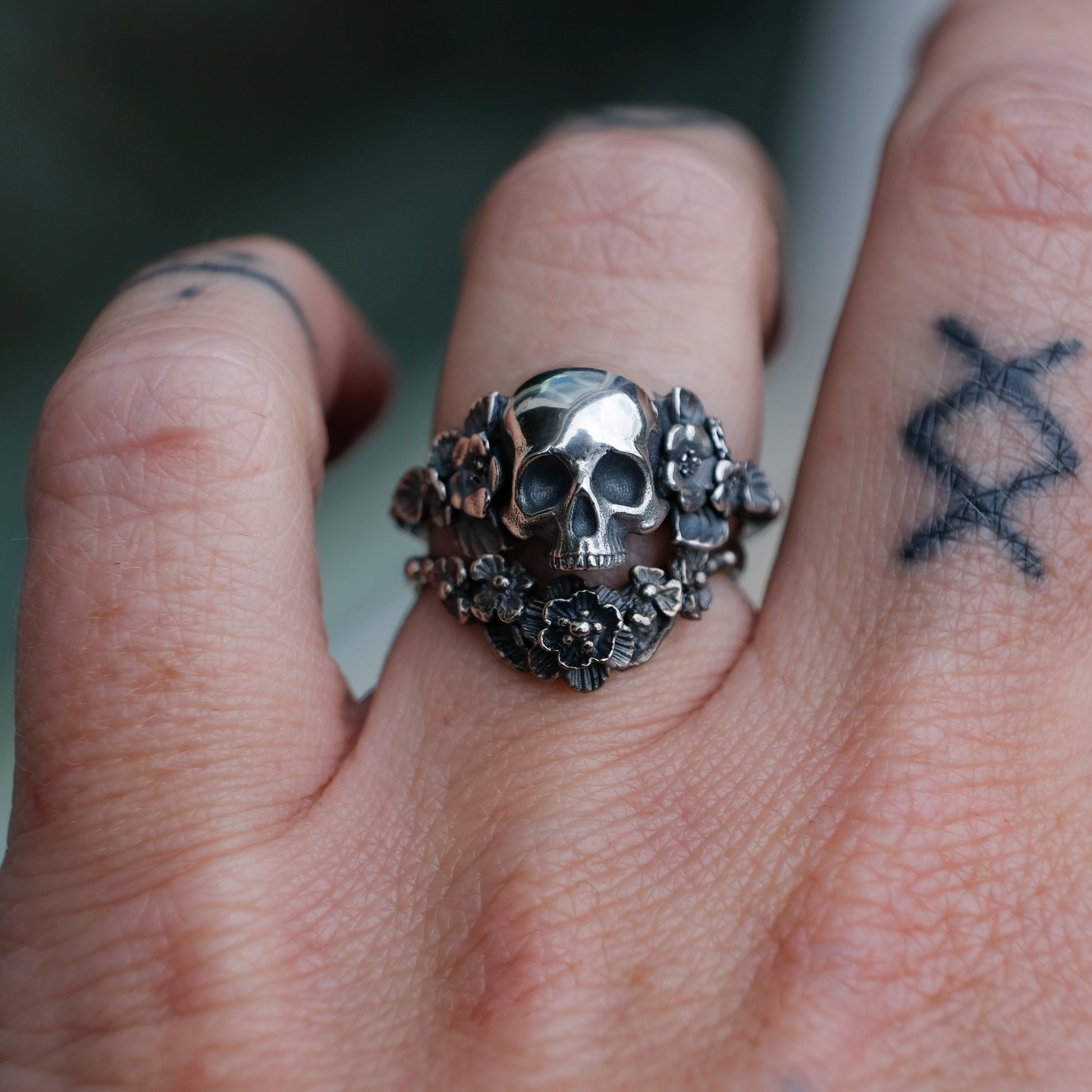Sterling silver ring with central large skull and flower and leaves cascading down band. Handmade in London by Charlie Shires