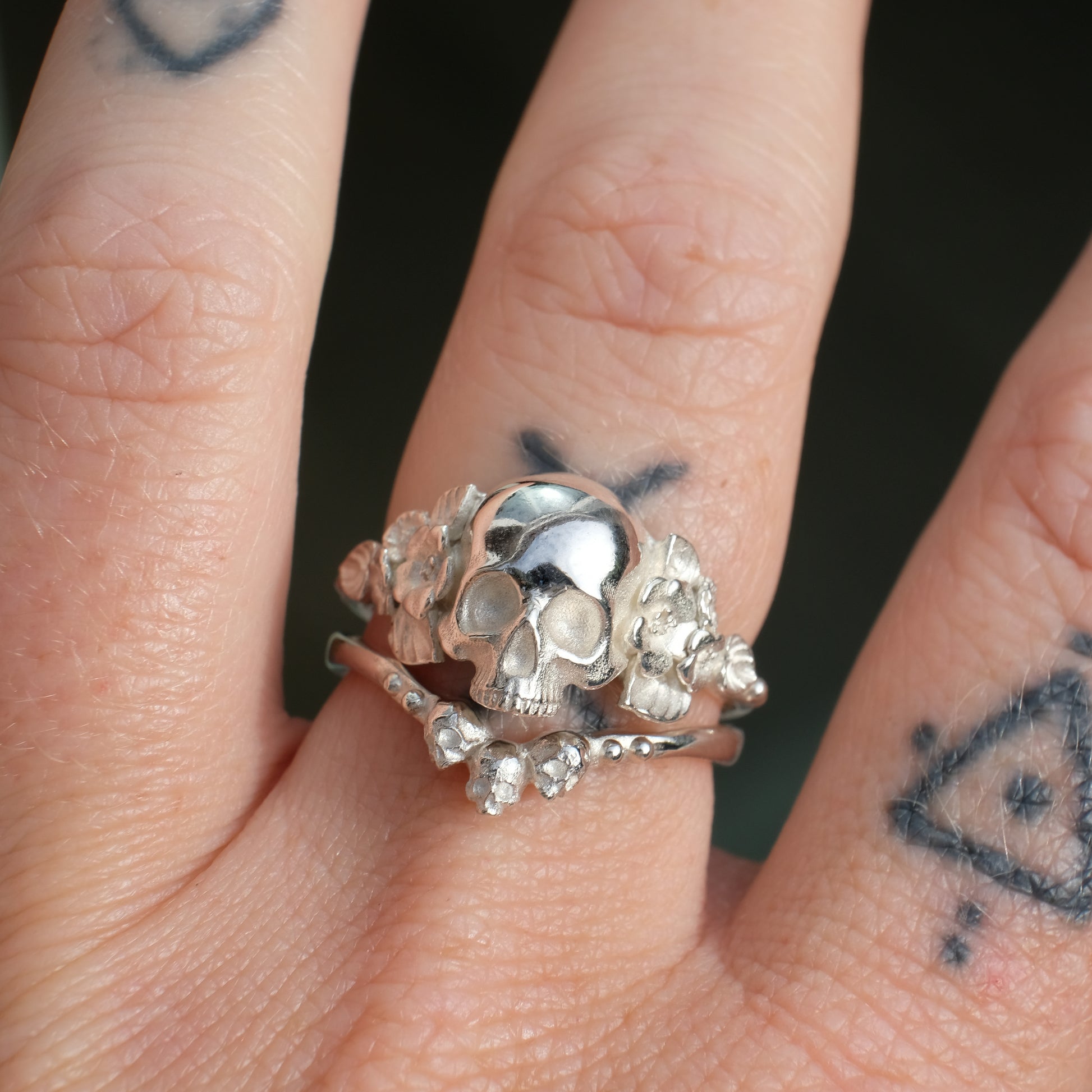 Sterling silver ring with central large skull and flower and leaves cascading down band. Handmade in London by Charlie Shires
