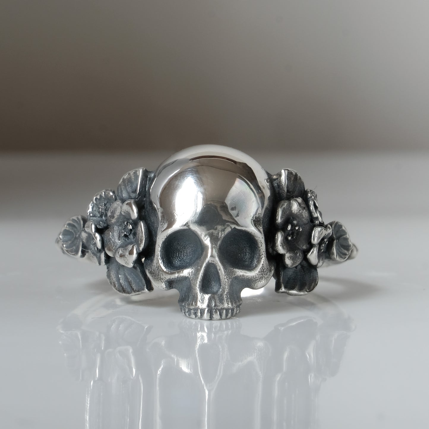 Sterling silver ring with central large skull and flower and leaves cascading down band. Handmade in London by Charlie Shires