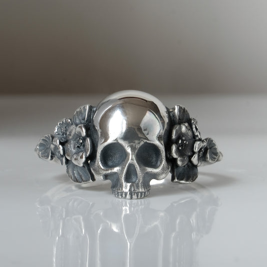 Sterling silver ring with central large skull and flower and leaves cascading down band. Handmade in London by Charlie Shires
