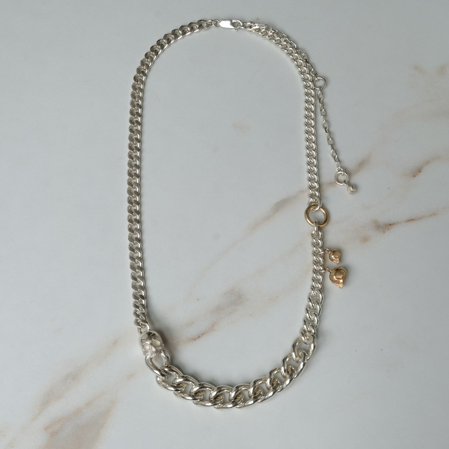 Heavy weight sterling silver curb link chain descending in size. 9ct yellow gold skulls hang off center from links. Handmade in London by Charlie Shires