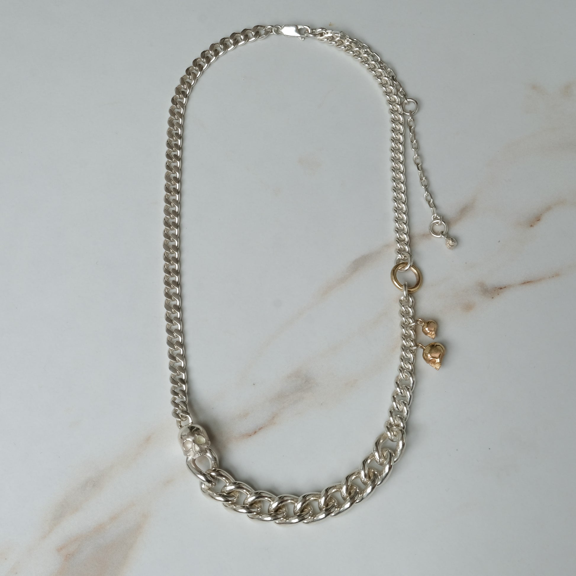 Heavy weight sterling silver curb link chain descending in size. 9ct yellow gold skulls hang off center from links. Handmade in London by Charlie Shires