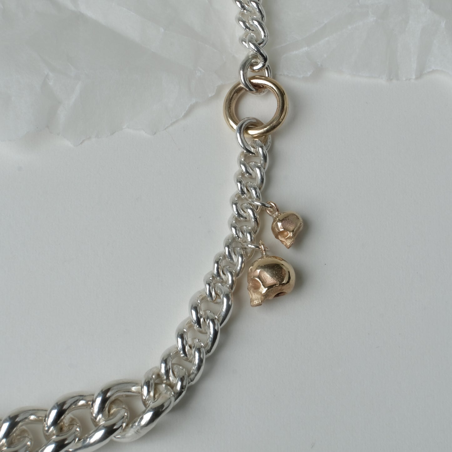 Heavy weight sterling silver curb link chain descending in size. 9ct yellow gold skulls hang off center from links. Handmade in London by Charlie Shires