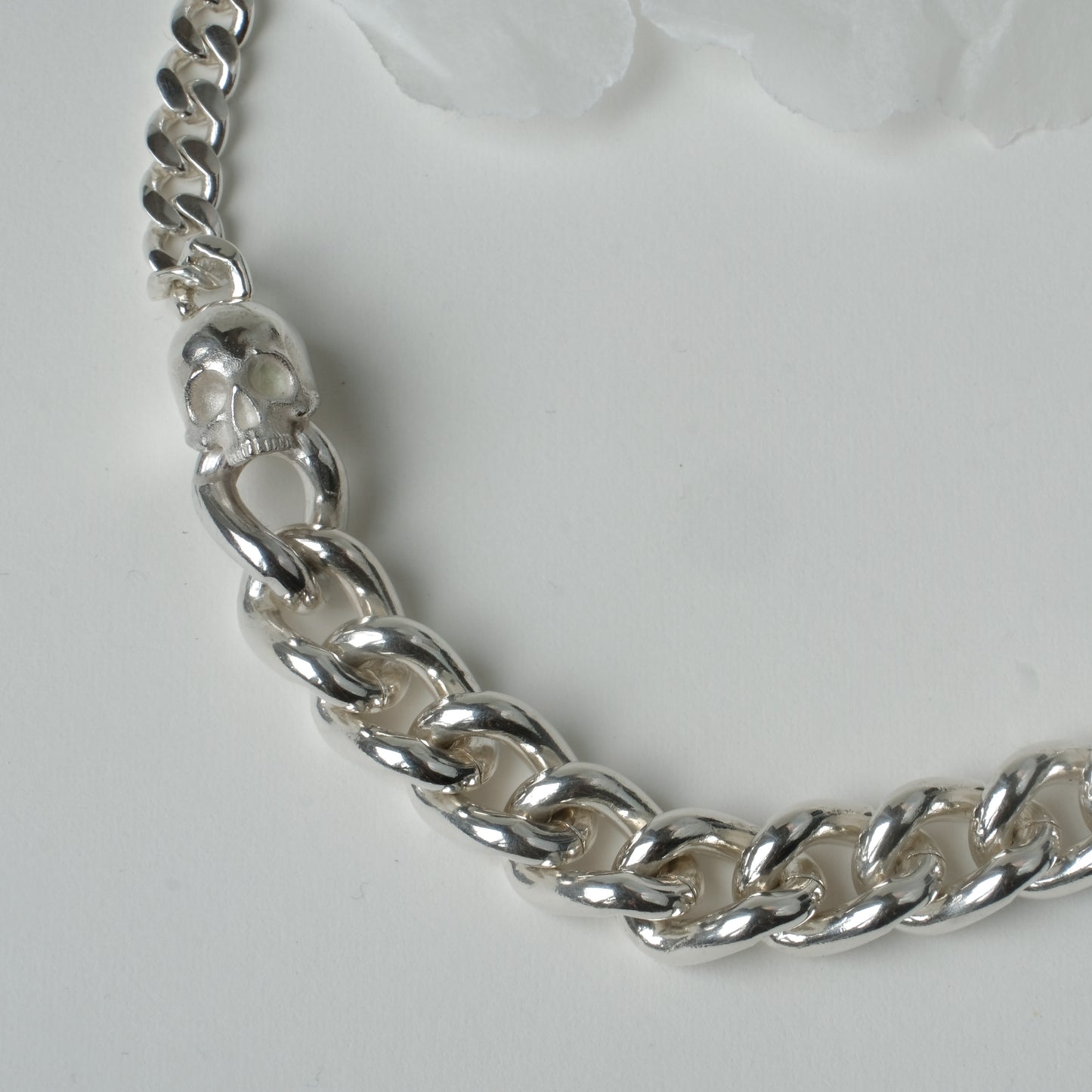 Heavy weight sterling silver curb link chain descending in size. 9ct yellow gold skulls hang off center from links. Handmade in London by Charlie Shires