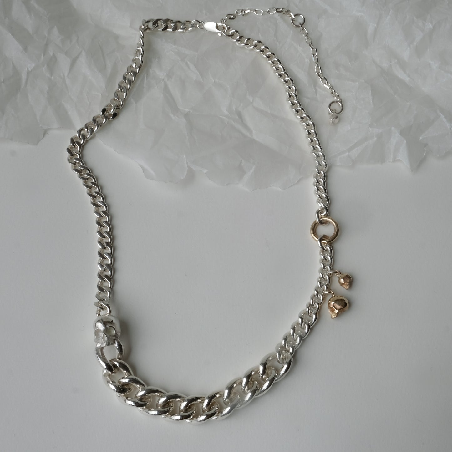Heavy weight sterling silver curb link chain descending in size. 9ct yellow gold skulls hang off center from links. Handmade in London by Charlie Shires