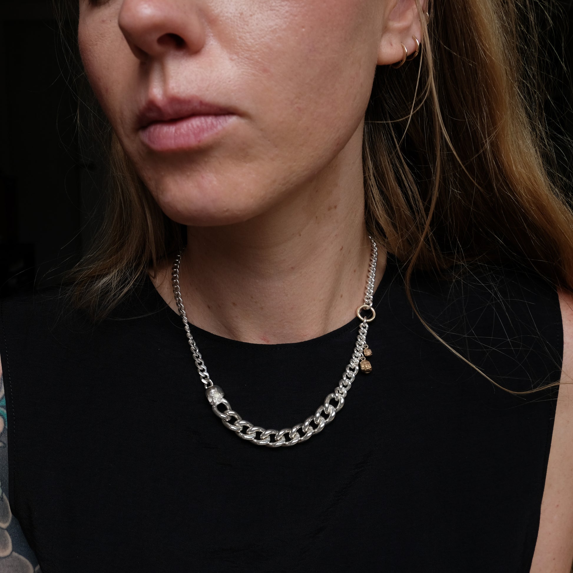 Heavy weight sterling silver curb link chain descending in size. 9ct yellow gold skulls hang off center from links. Handmade in London by Charlie Shires