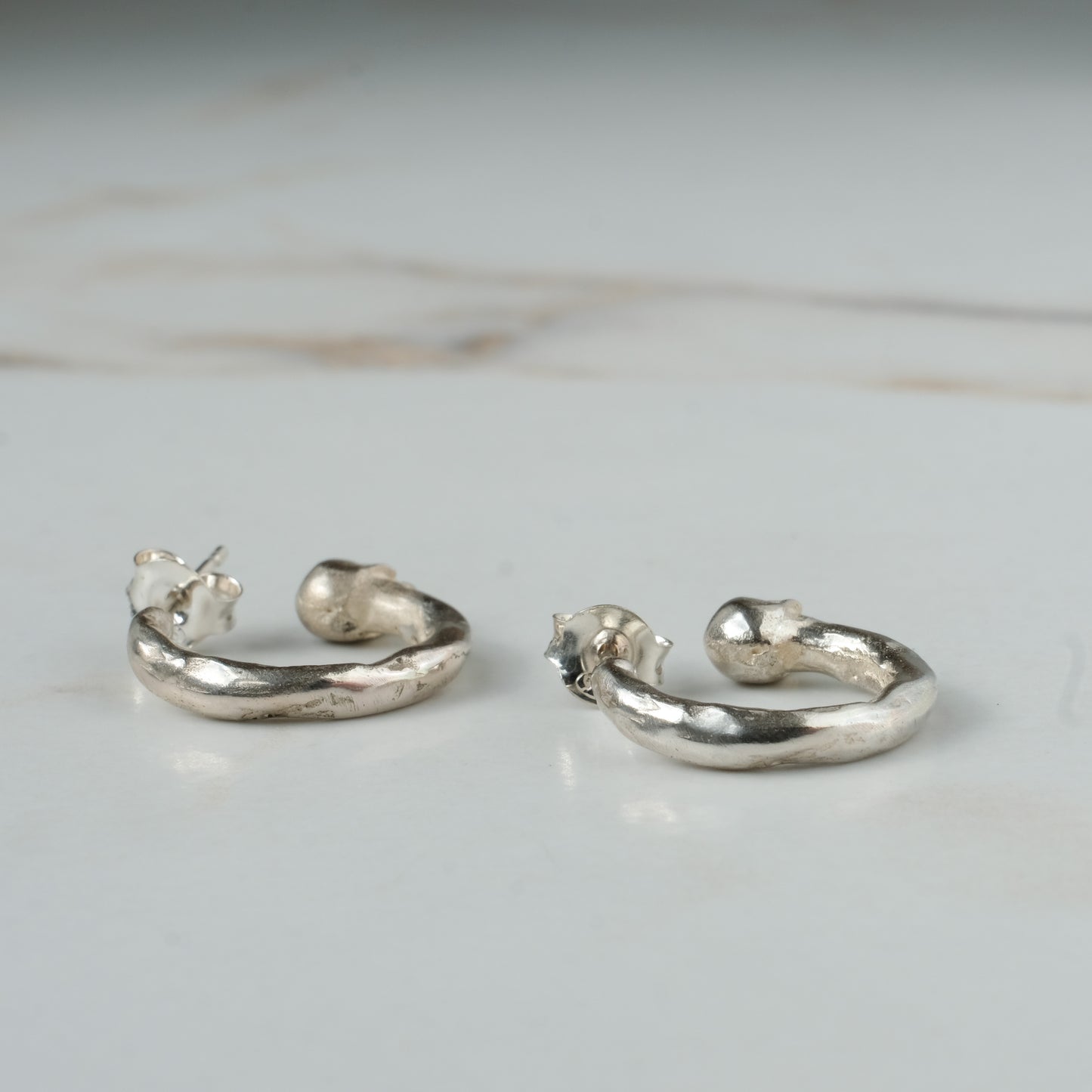 Small hoop earrings with molten detail and skulls at back in sterling silver by Charlie Shires