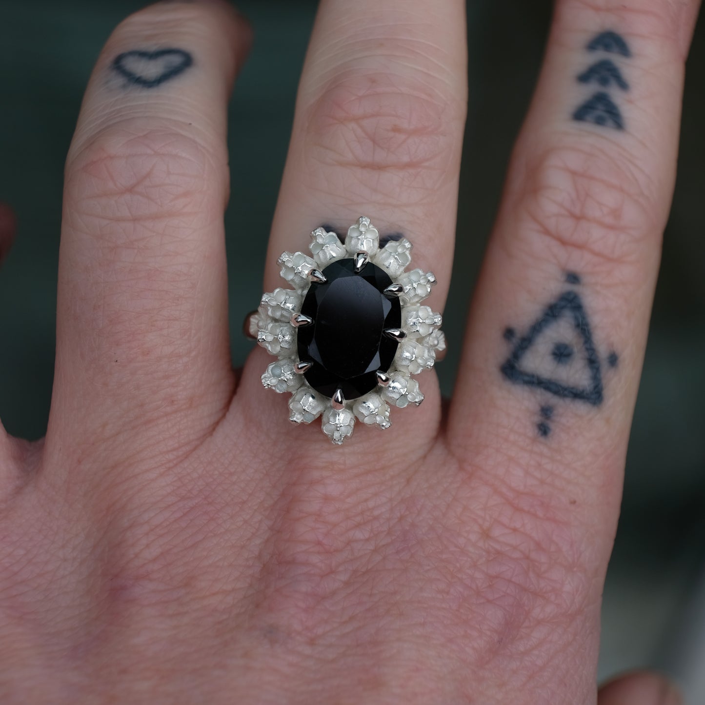 Ring with claw set black spinel gemstone and silver skull design worn on hand with tattoos with neutral background