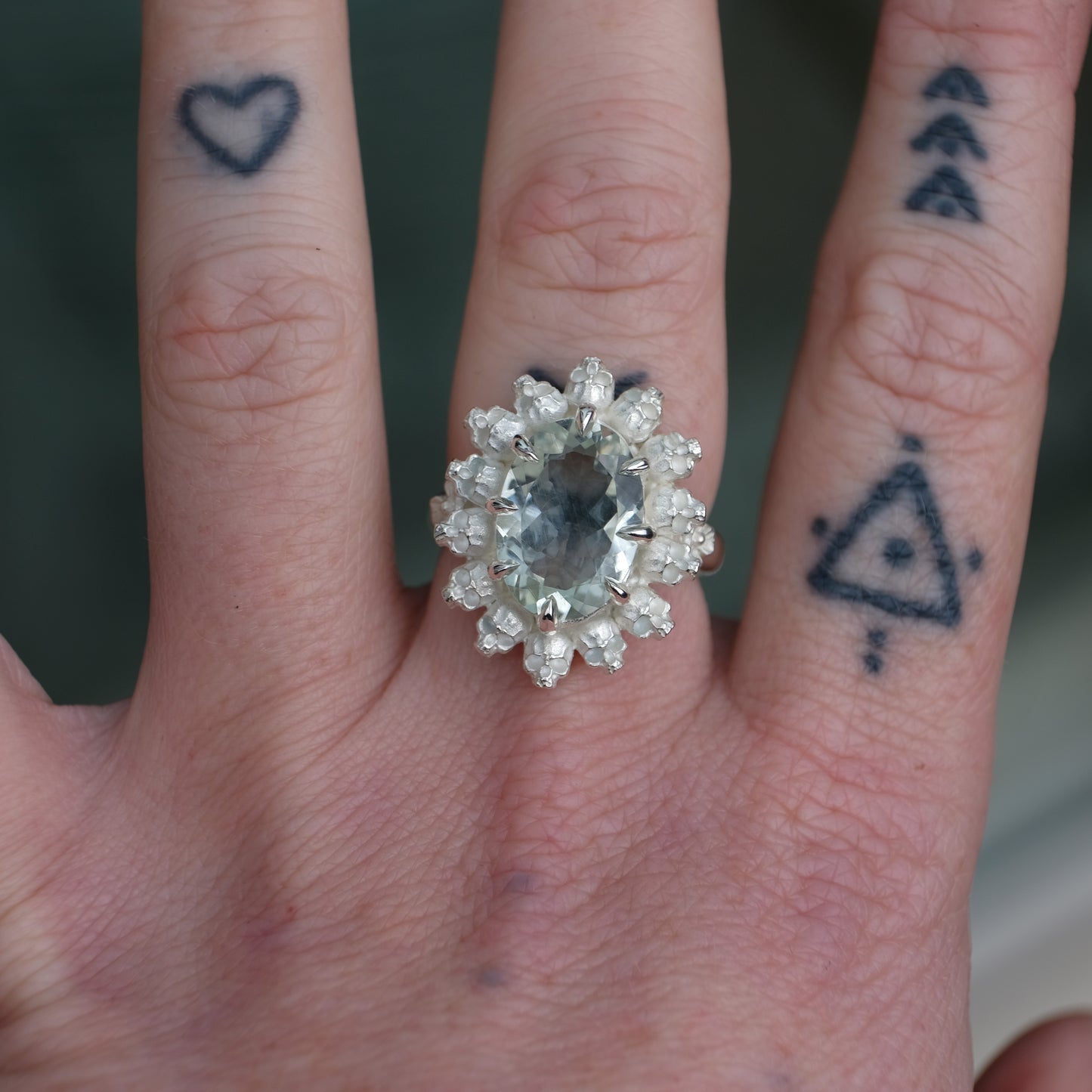Ring with claw set mint quartz gemstone and silver skull design worn on tattooed had with neutral background