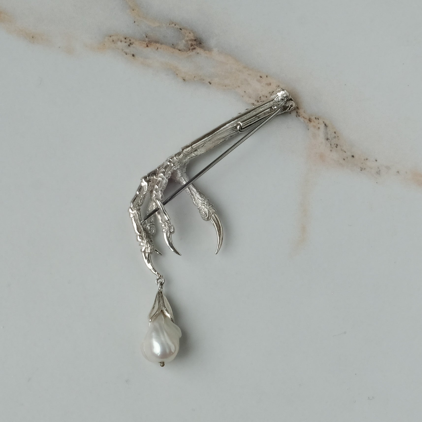 Birds claw talon brooch made in sterling silver with drop freshwater pearl. Made in London by Charlie Shires