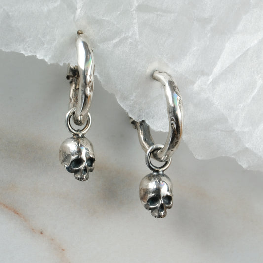 Molten style sterling silver earrings with hidden skull stoppers and skulls hanging. Made in London by Charlie Shires