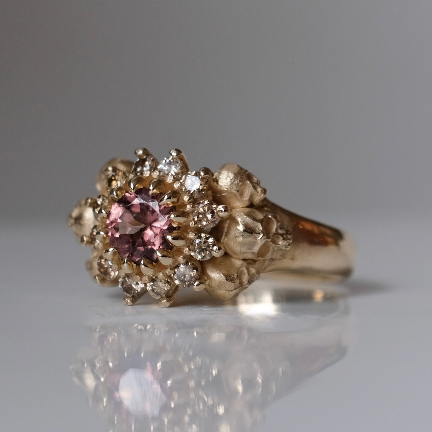 9ct yellow gold engagement ring with central colour change garnet and a champagne diamond halo. 6 skulls flank the side of the setting. 
Handmade in London by Charlie Shires