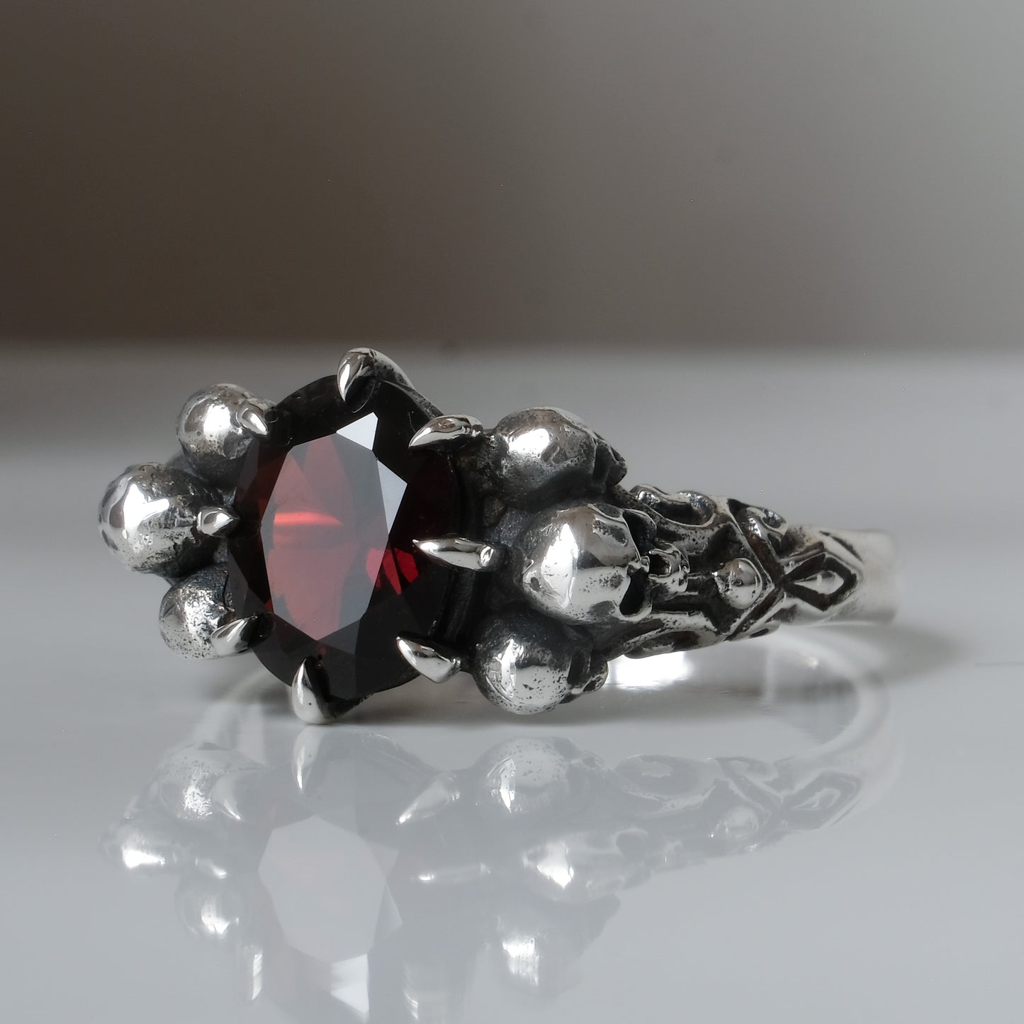 Three skull ring with central garnet and decorative band by Charlie Shires