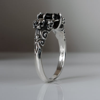 Three skull ring with central garnet and decorative band by Charlie Shires