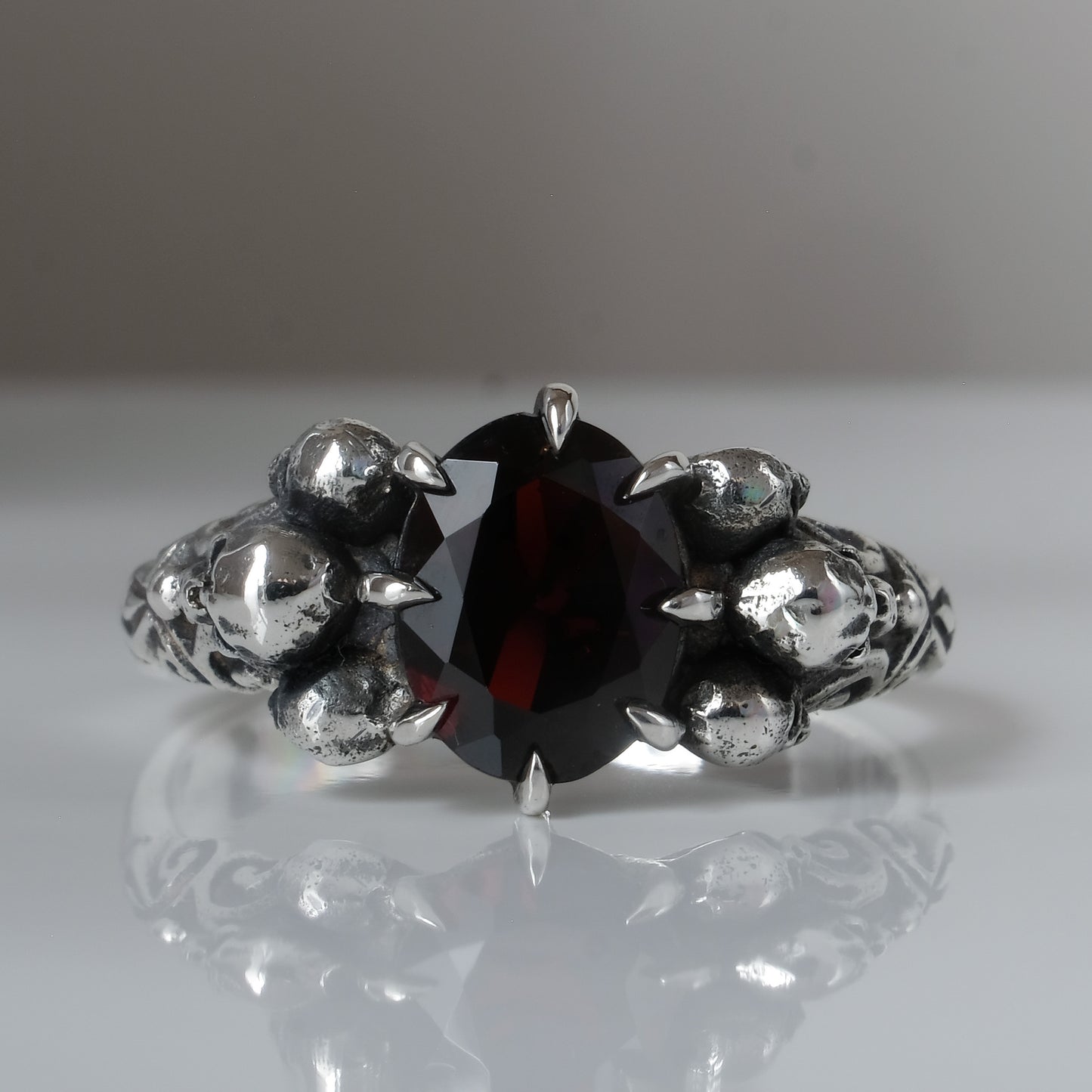 Three skull ring with central garnet and decorative band by Charlie Shires
