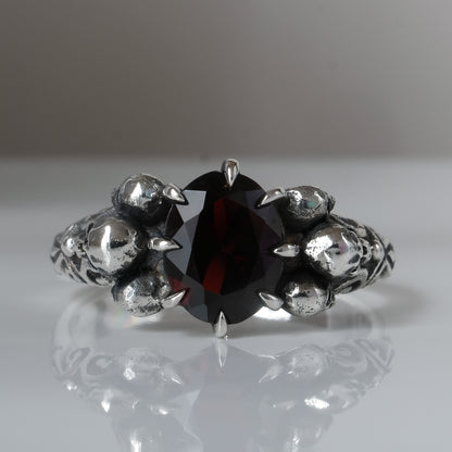 Three skull ring with central garnet and decorative band by Charlie Shires