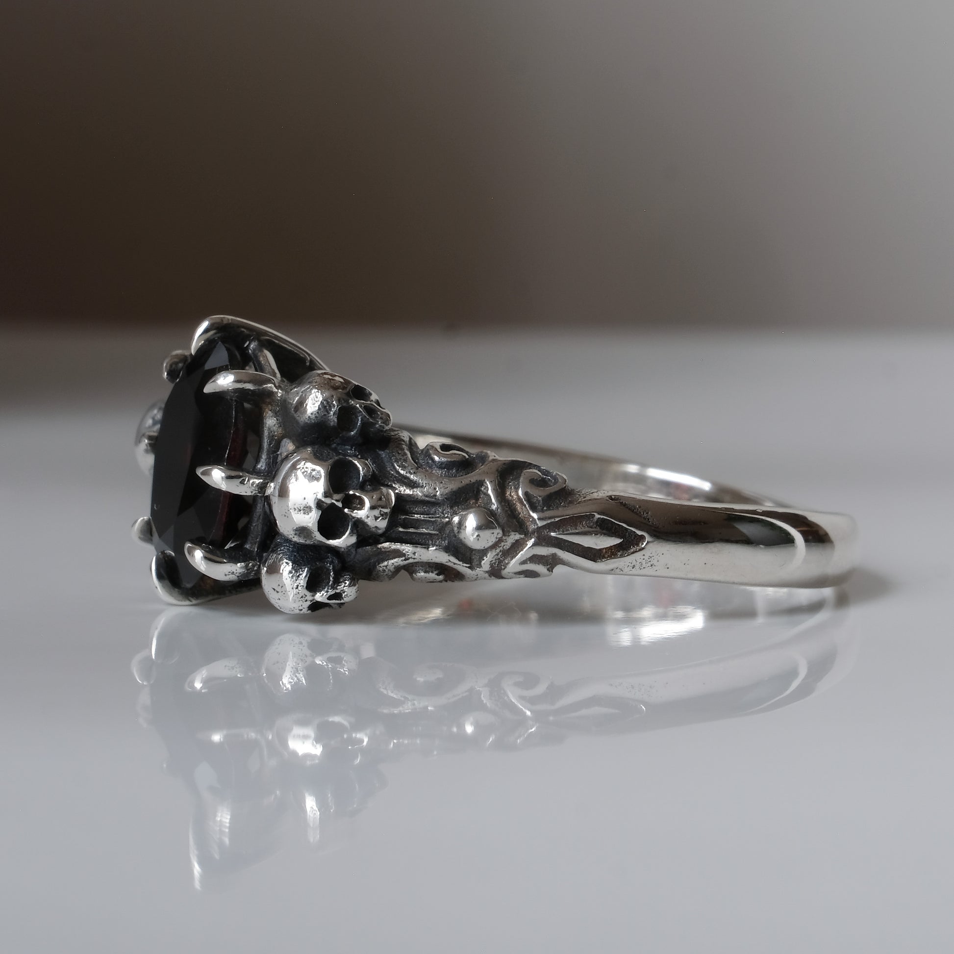 Three skull ring with central garnet and decorative band by Charlie Shires