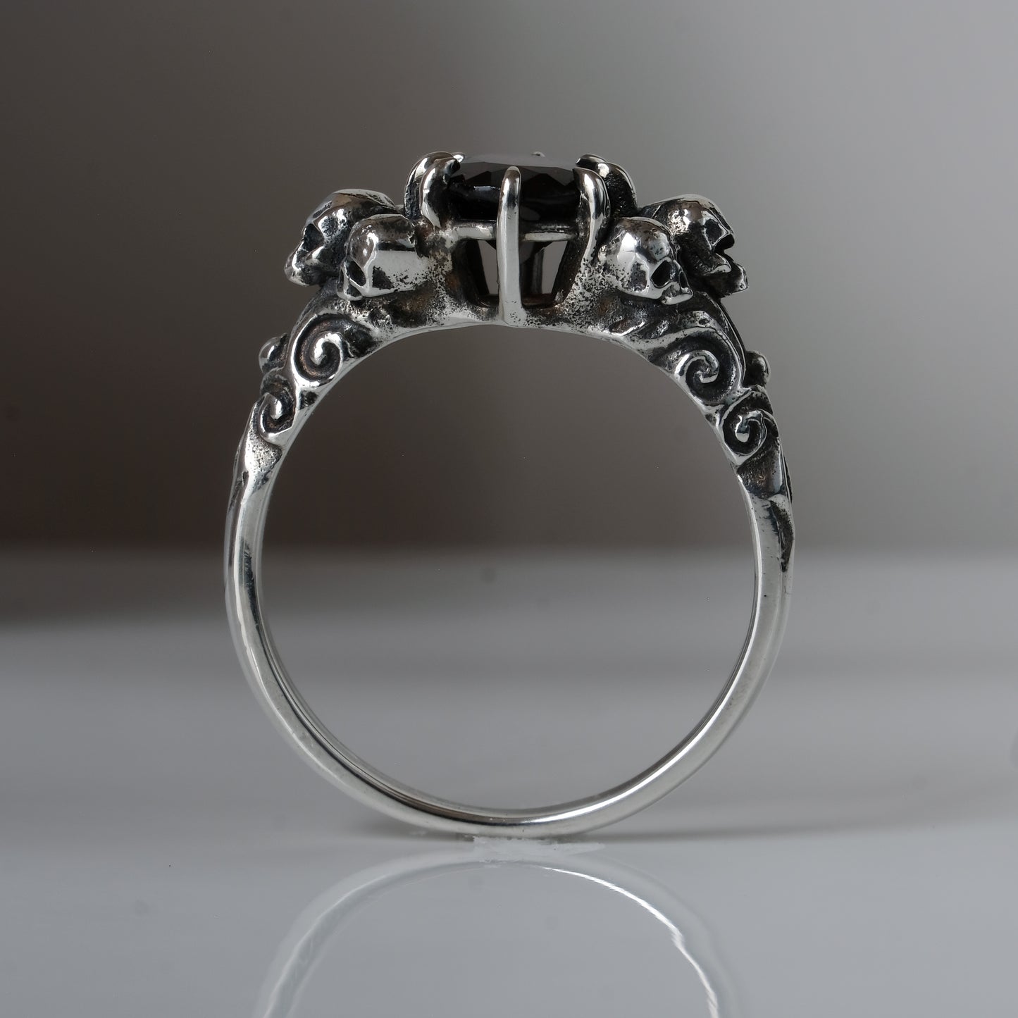 Three skull ring with central garnet and decorative band by Charlie Shires