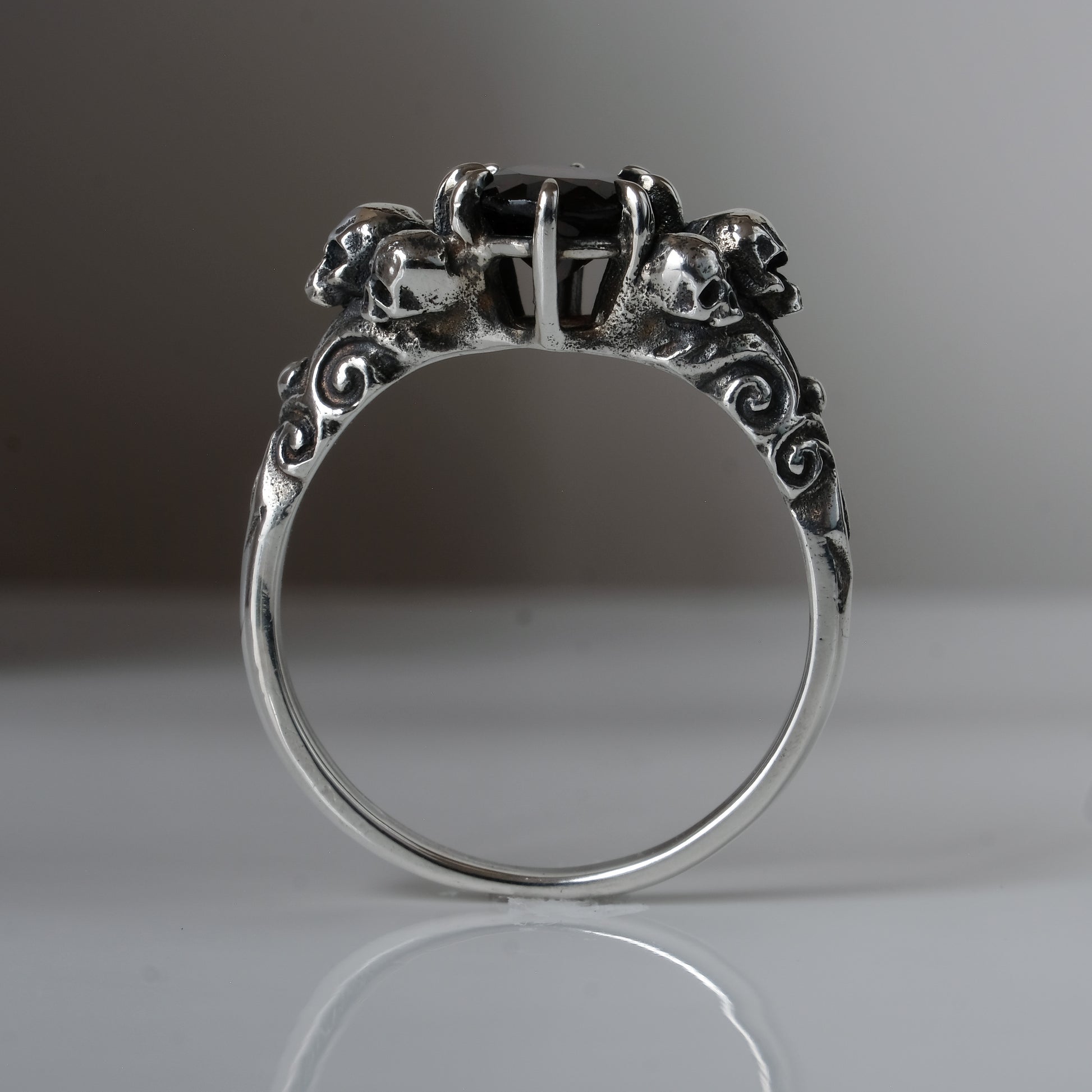 Three skull ring with central garnet and decorative band by Charlie Shires