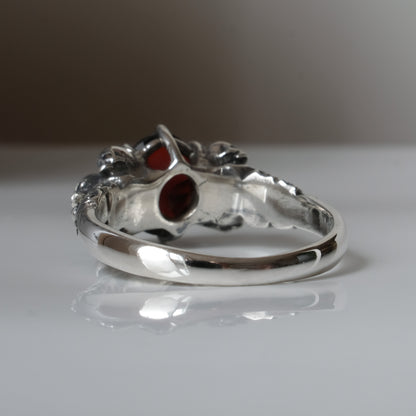 Three skull ring with central garnet and decorative band by Charlie Shires