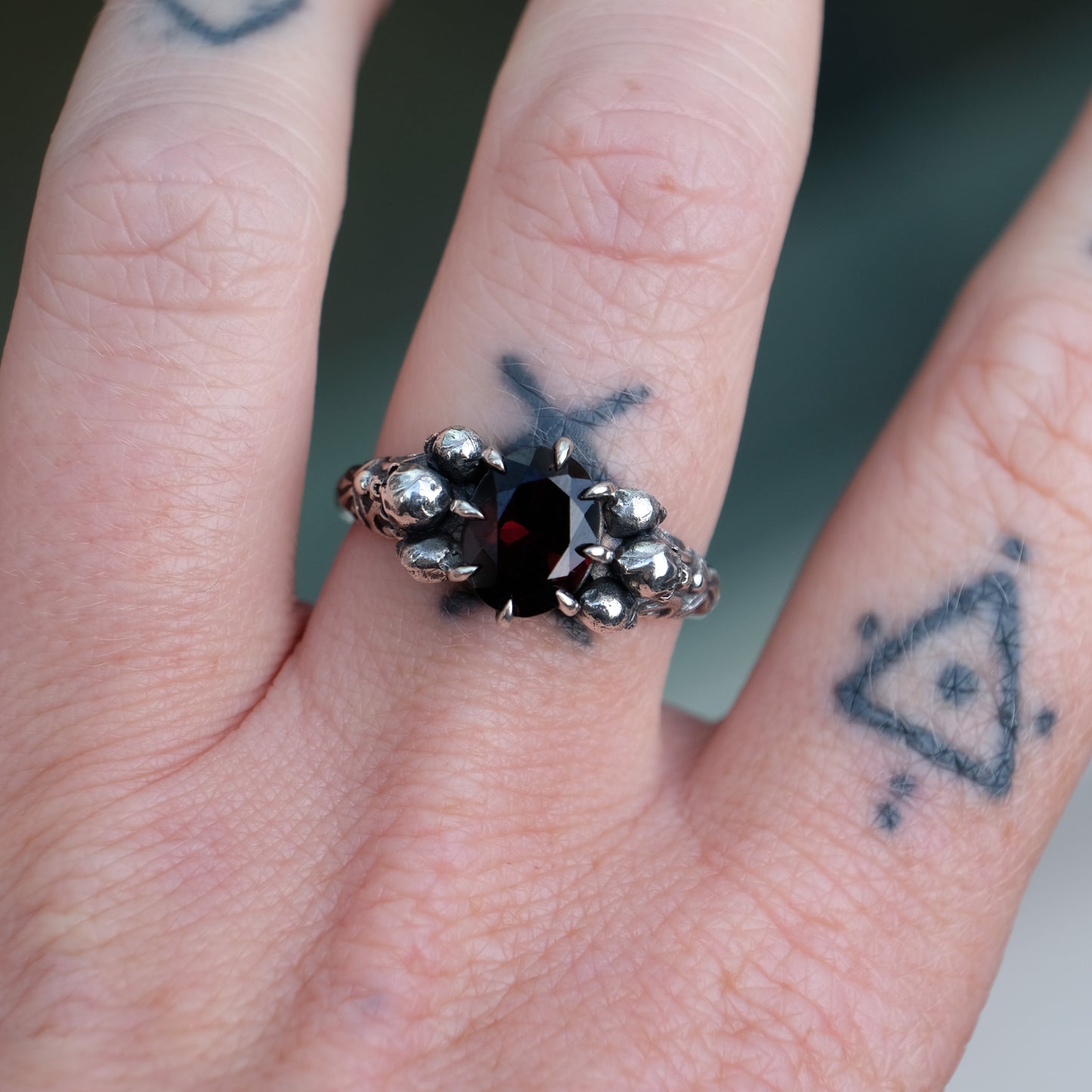 Three skull ring with central garnet and decorative band by Charlie Shires