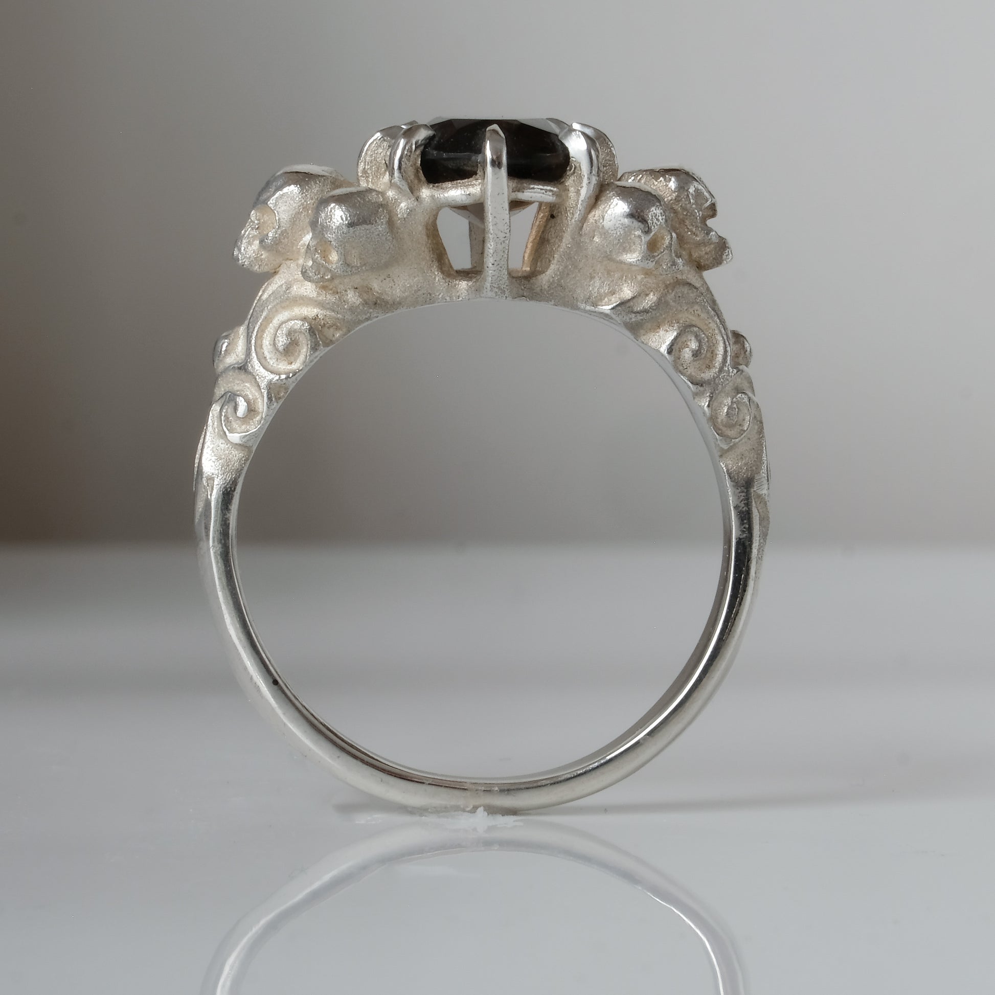 Three skull ring with central tourmaline and decorative band