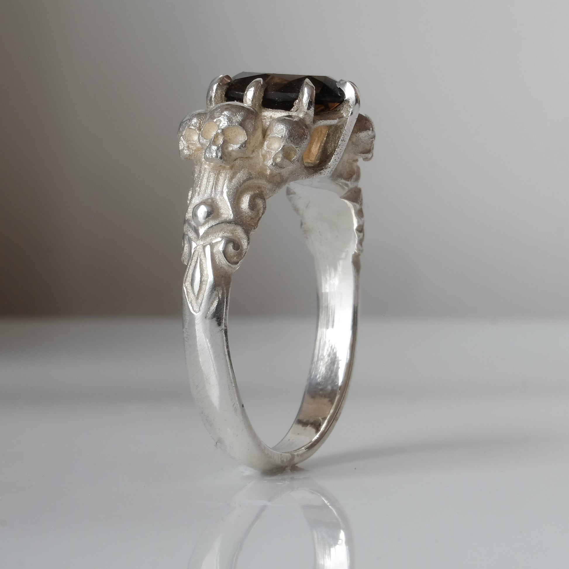 Three skull ring with central tourmaline and decorative band