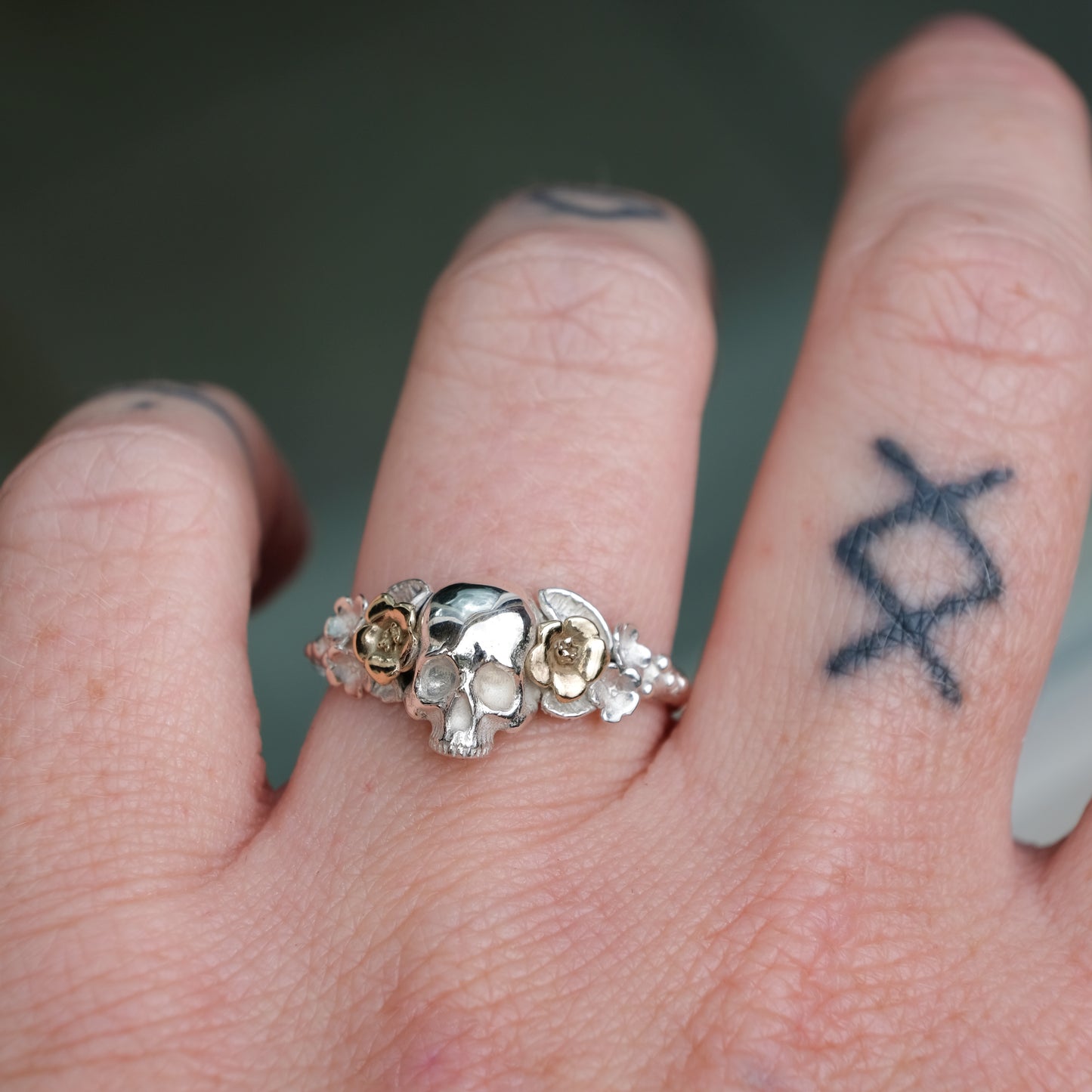 Sterling silver ring with central skull and 9ct yellow gold flower and leaves cascading down band. Handmade in London by Charlie Shires
