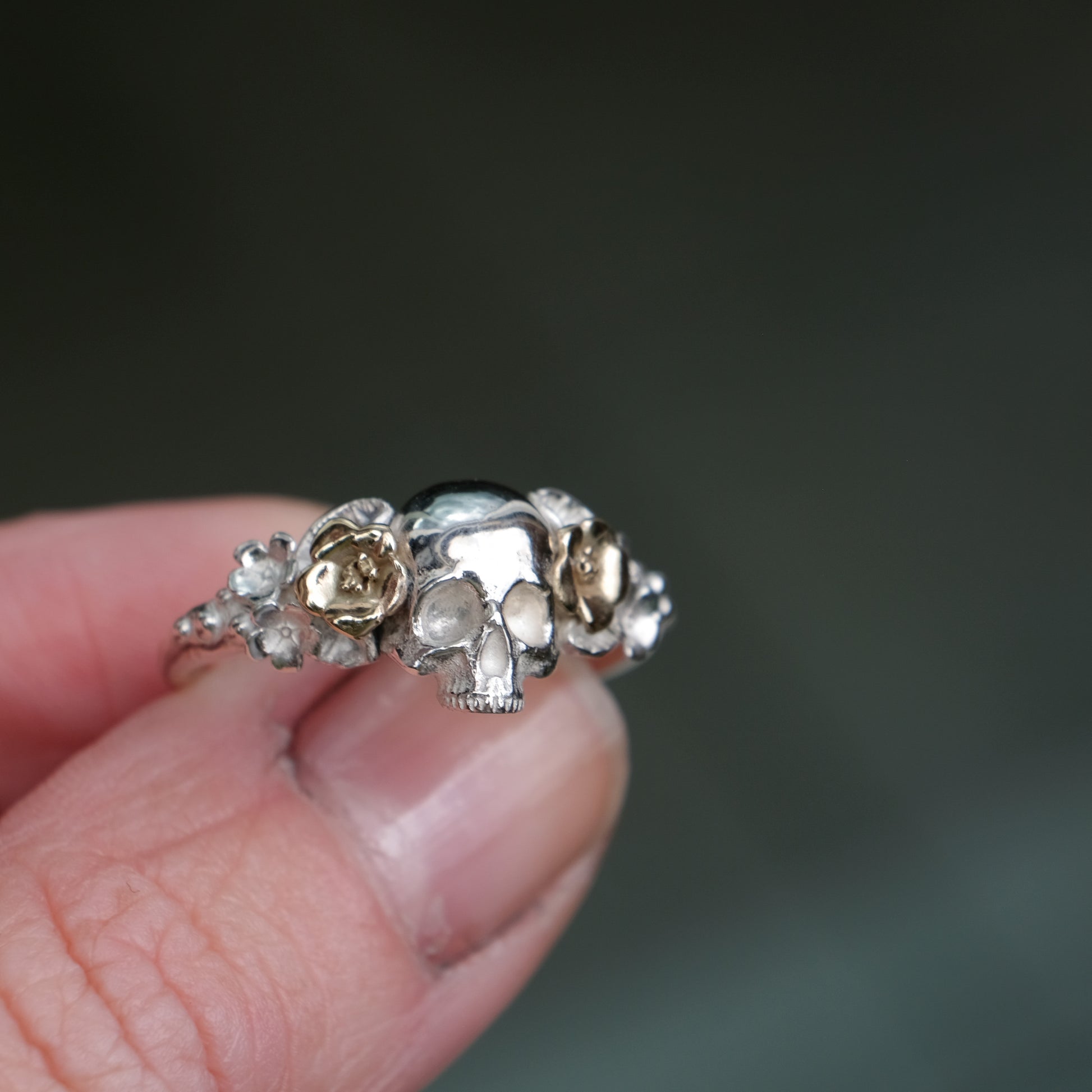 Sterling silver ring with central skull and 9ct yellow gold flower and leaves cascading down band. Handmade in London by Charlie Shires