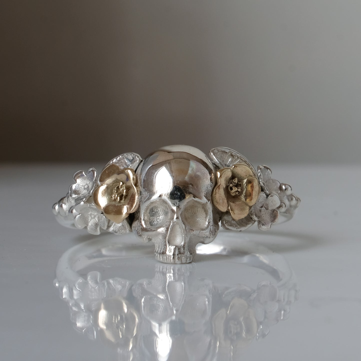 Sterling silver ring with central skull and 9ct yellow gold flower and leaves cascading down band. Handmade in London by Charlie Shires