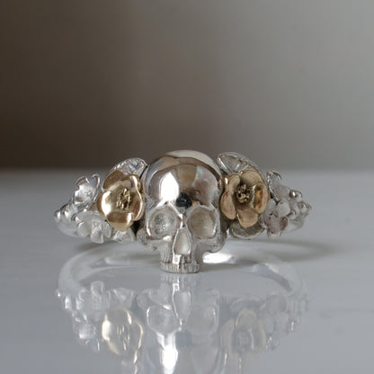 Sterling silver ring with central skull and 9ct yellow gold flower and leaves cascading down band. Handmade in London by Charlie Shires