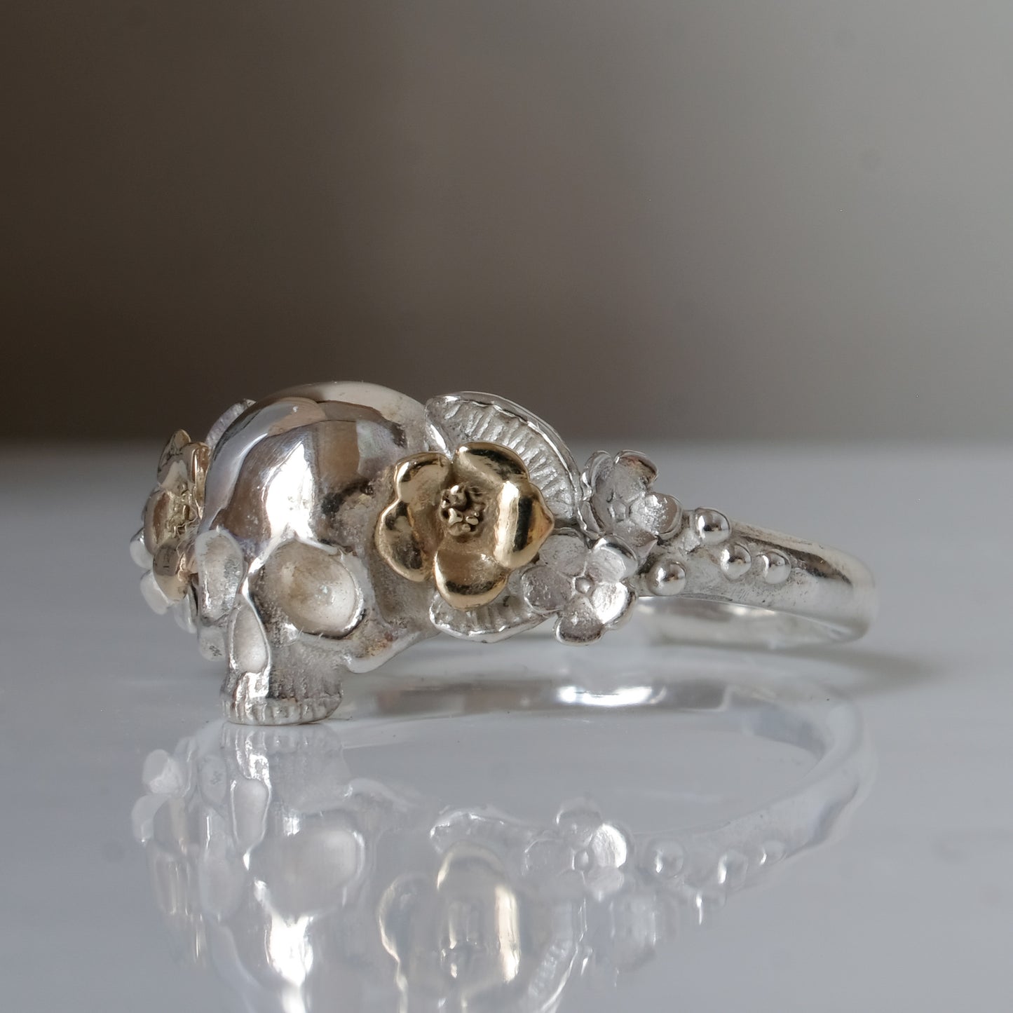 Sterling silver ring with central skull and 9ct yellow gold flower and leaves cascading down band. Handmade in London by Charlie Shires