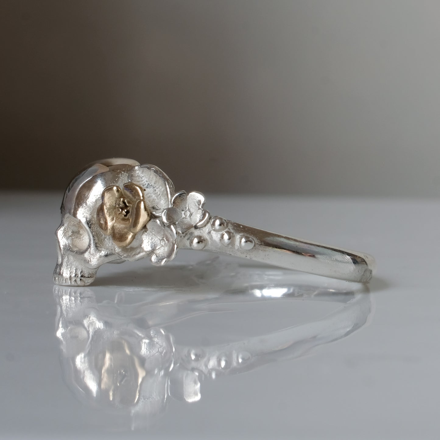 Sterling silver ring with central skull and 9ct yellow gold flower and leaves cascading down band. Handmade in London by Charlie Shires