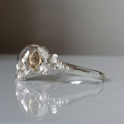 Sterling silver ring with central skull and 9ct yellow gold flower and leaves cascading down band. Handmade in London by Charlie Shires
