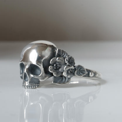 Sterling silver ring with central large skull and flower and leaves cascading down band. Handmade in London by Charlie Shires