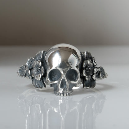 Sterling silver ring with central large skull and flower and leaves cascading down band. Handmade in London by Charlie Shires