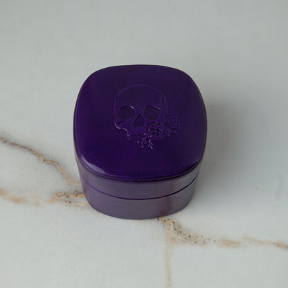 A purple leather engagement ring box with an embossed skull logo by Charlie Shires