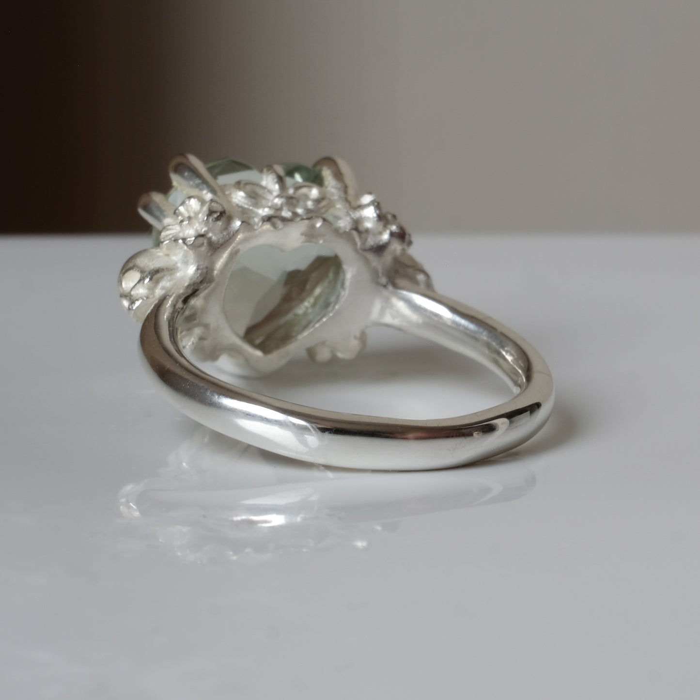 Silver ring with a heart-shaped green mint quartz gemstone decorated with skulls and flowers on a white surface