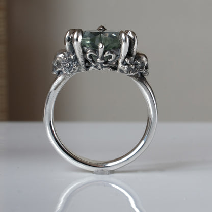 Silver ring with a heart-shaped green mint quartz gemstone decorated with skulls and flowers on a white surface